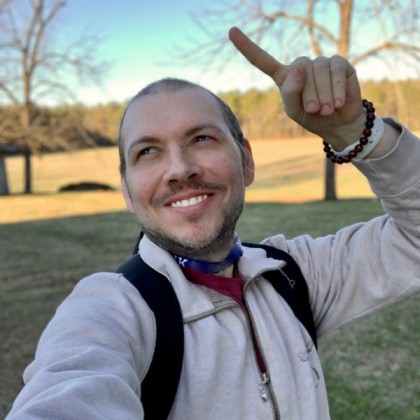 Curtis Garbett standing outside smiling and pointing toward the sky